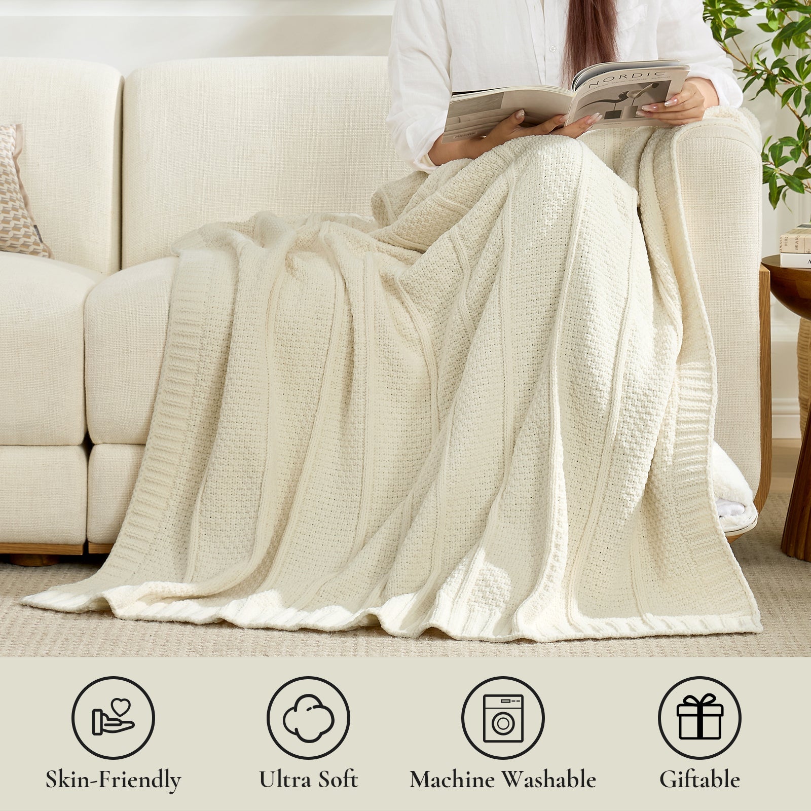 Woman sitting on a couch with an Ivory blanket draped over her, reading a book. #color_Ivory