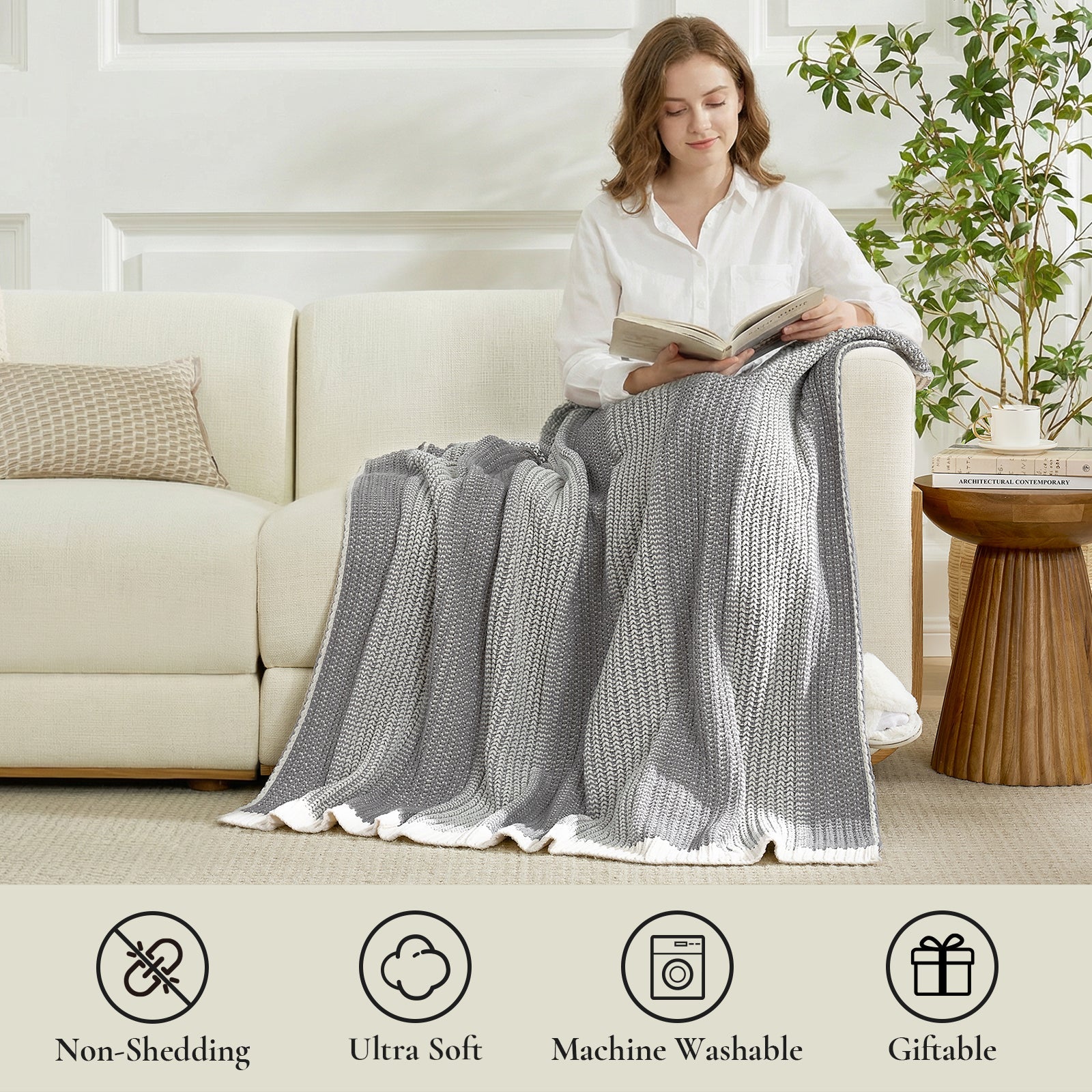 Woman sitting on a couch with a Snuggle Sac grey blanket, reading a book, in a cozy living room setting. #color_Two-tone Grey