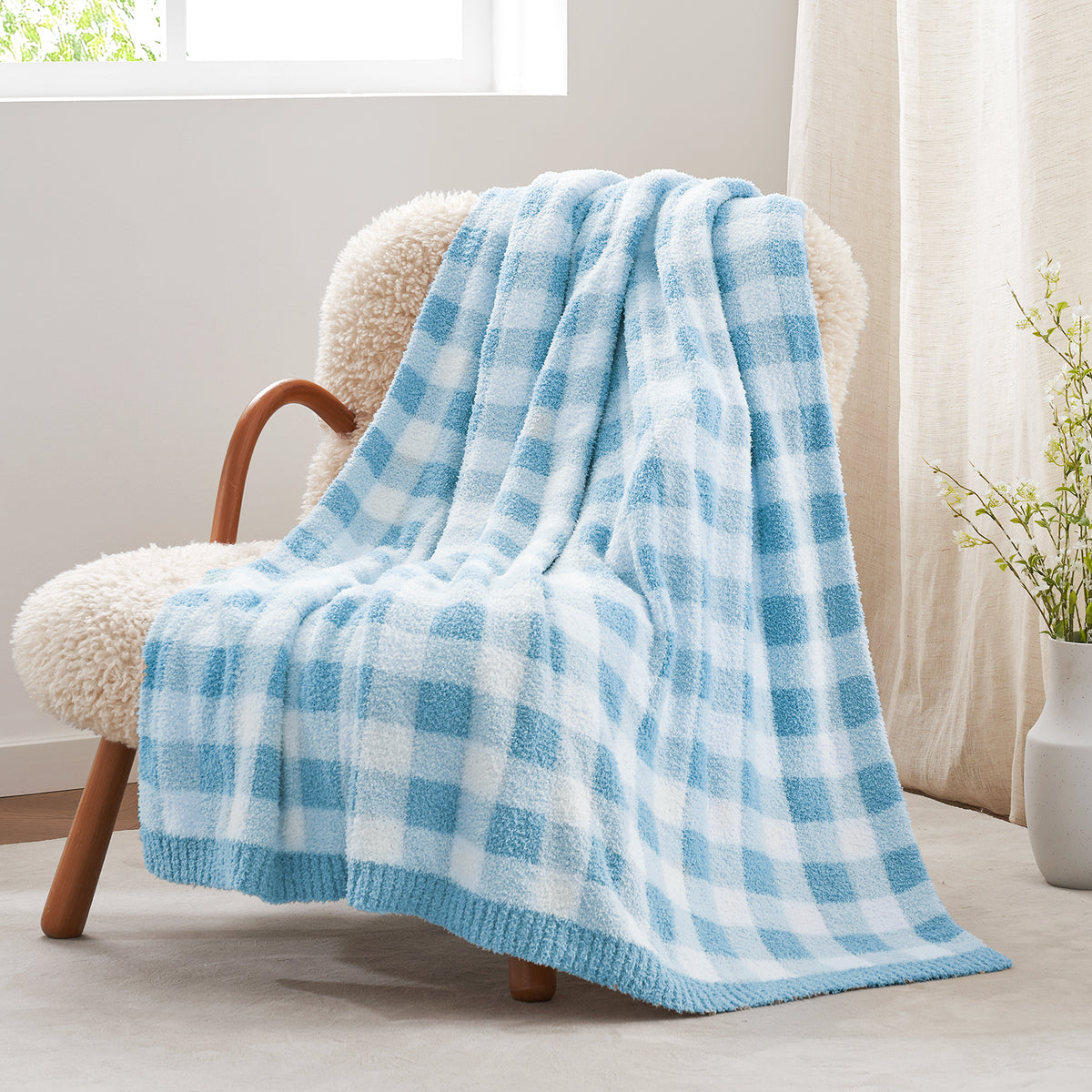 Blue and white checkered blanket draped over a chair in a bright room with a vase of flowers#color_Ice Blue