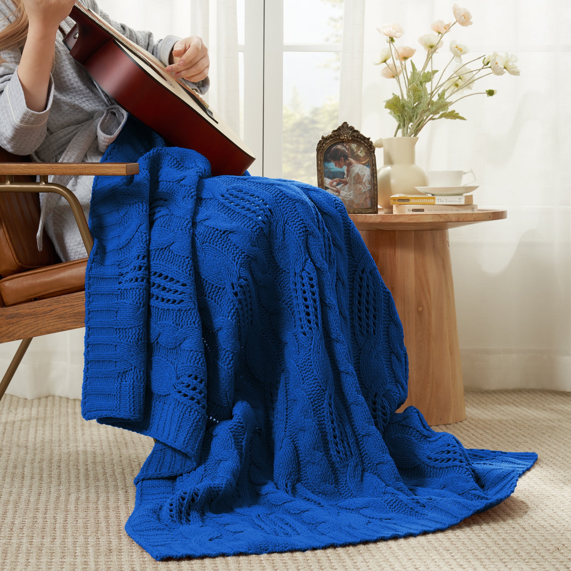 Woman sitting on chair with a Snuggle Sac cable chenille knit throw blanket in Navy Blue while playing guitar #color_Navy Blue