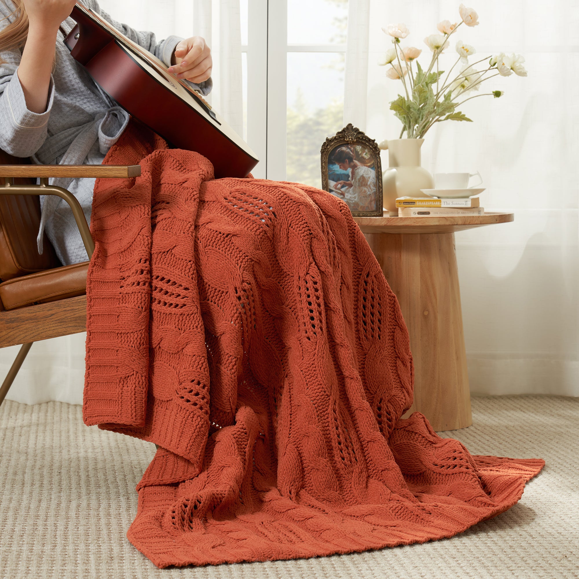 Woman sitting on chair with a cable chenille knit throw blanket in Burnt Orange while playing guitar #color_Burnt Orange