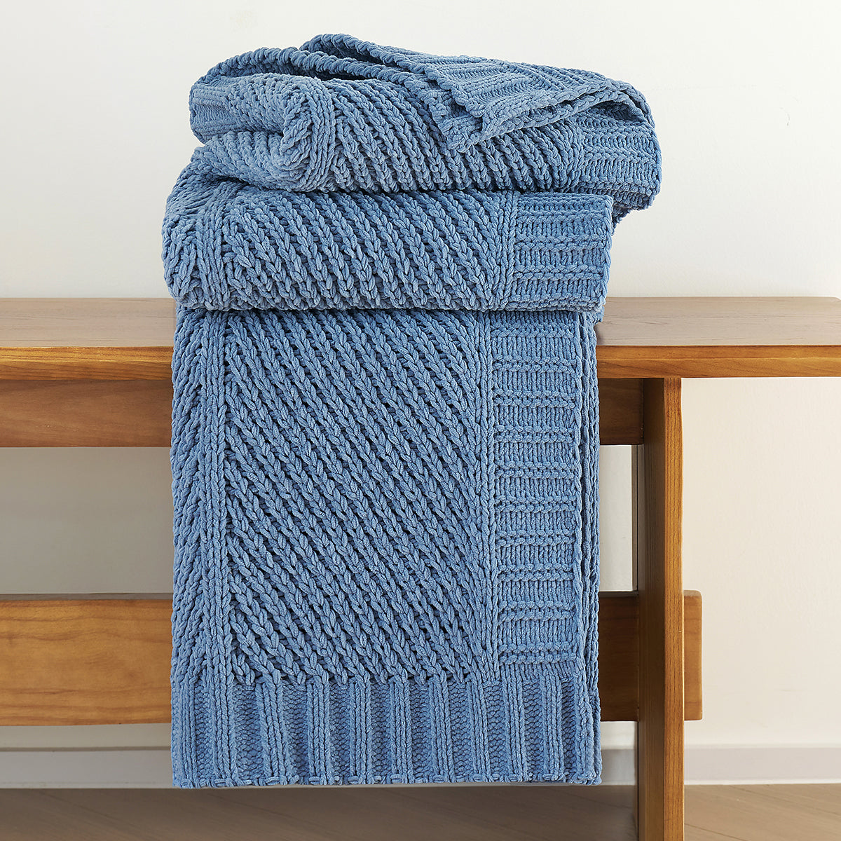 Neatly folded chenille knit throw blanket in Blue stacked on a bench showcasing thickness #color_Blue