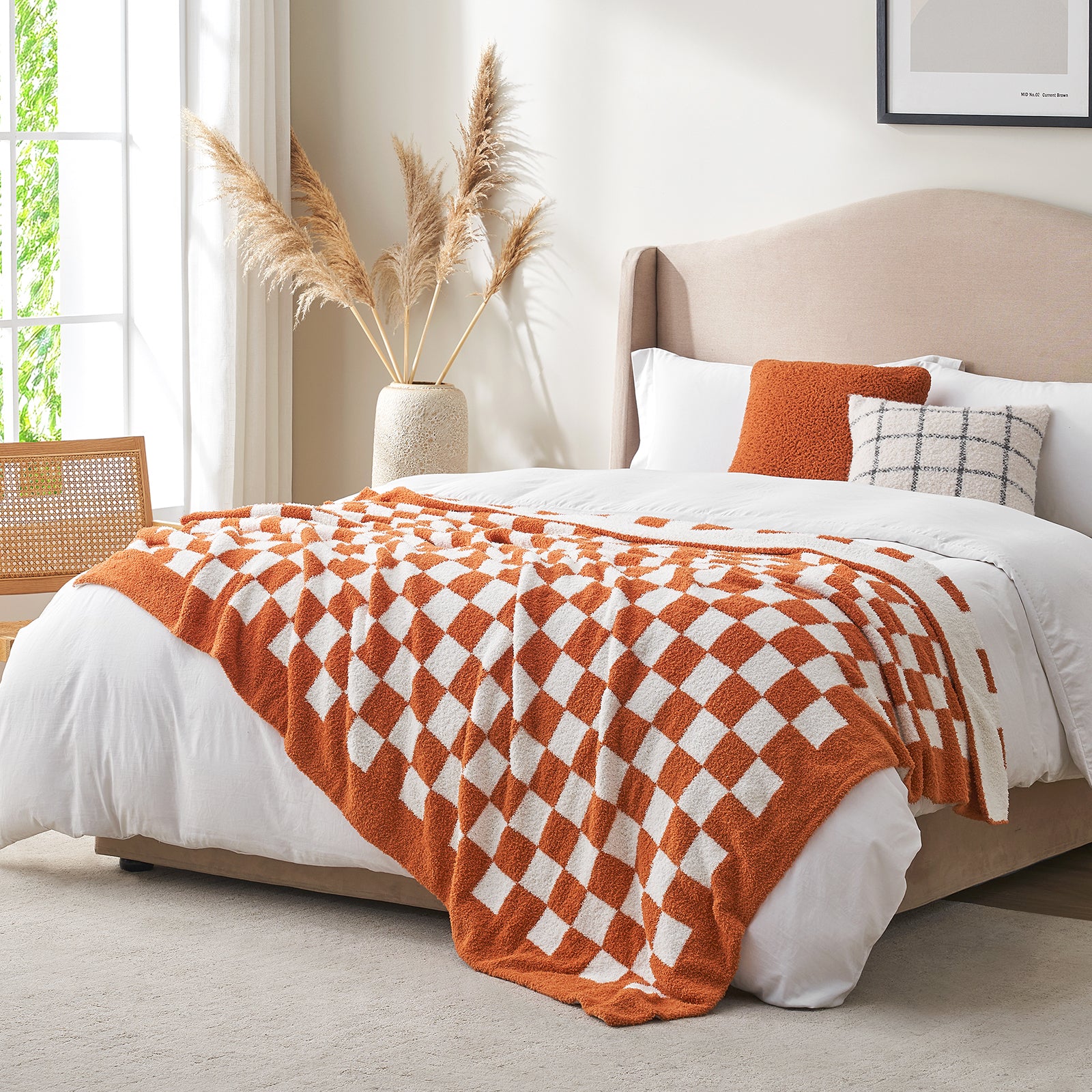Bedroom with a bed featuring an orange and white checkered blanket, pillows, and a vase with pampas grass. #color_Checkered Burnt Orange