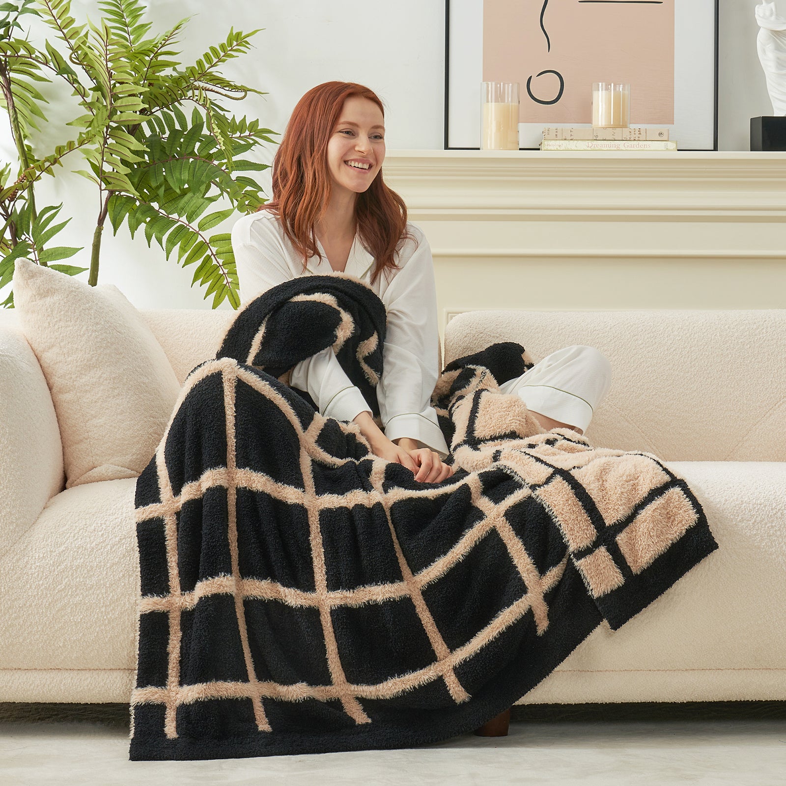 Woman sitting on a couch with a black and beige checkered faux fur knit throw blanket.#color_Black