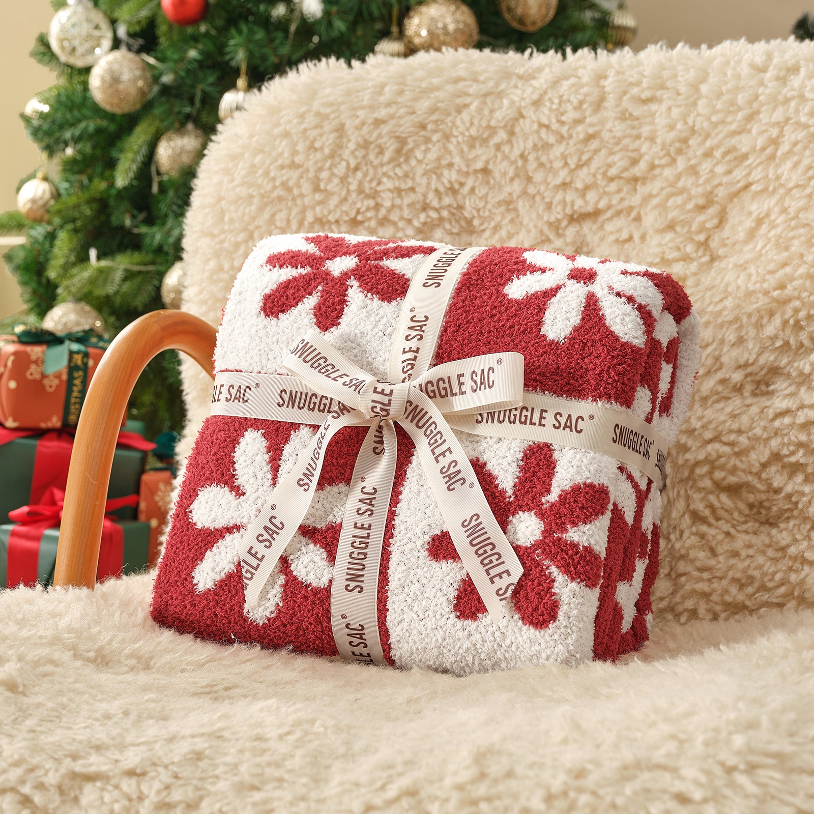 Red and white patterned Snuggle Sac on a beige surface with a Christmas tree in the background #color_Xmas Red