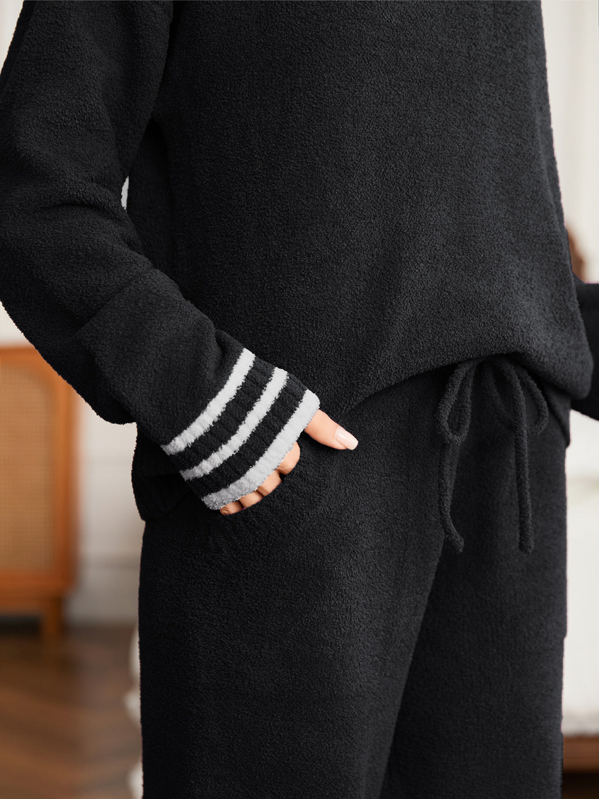 Person wearing a black sweater with striped cuffs and black pants in an indoor setting #color_Black