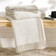 Snuggle Sac knitted beige blanket draped over a wooden surface with a neutral background #color_Khaki&White