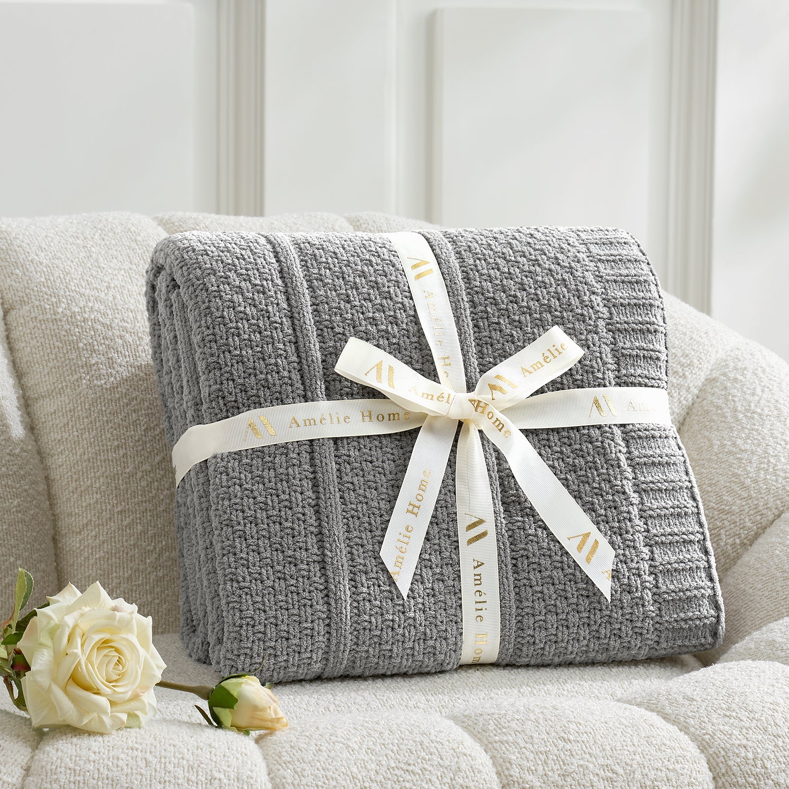 Gray textured blanket with a white ribbon on a light-colored sofa, accompanied by a white rose. #color_Gray