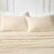Snuggle Sac Khaki quilted bedspread and pillows on a bed with a white headboard.#color_Khaki