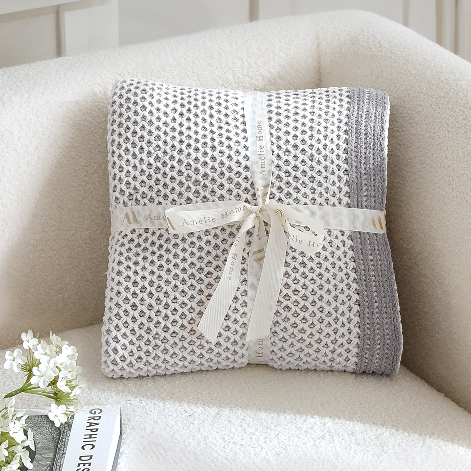 Folded textured blanket with a ribbon on a beige armchair #color_Gray&White