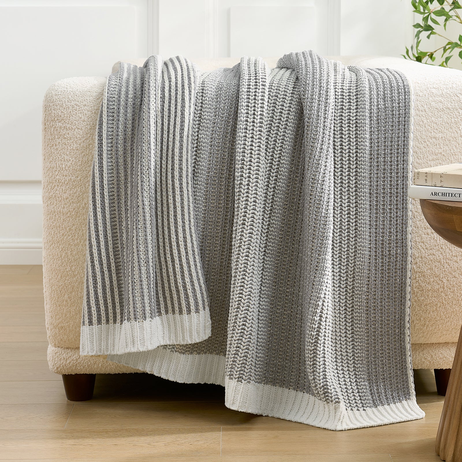 Snuggle Sac grey knitted blanket draped over a beige armchair in a room with light wood flooring and white walls. #color_Two-tone Grey
