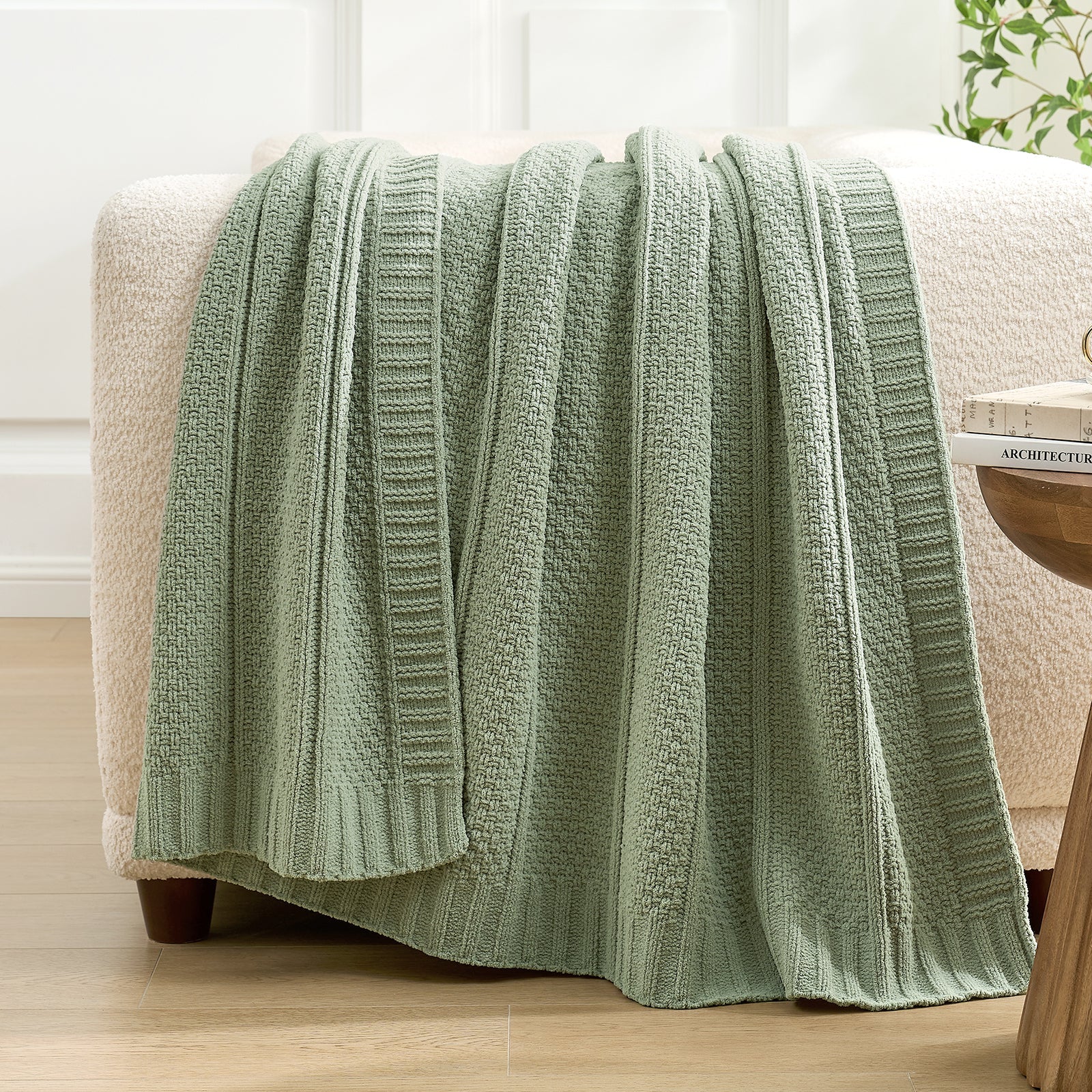 Green textured blanket draped over a white armchair in a room with light wood flooring. #color_Sage Green