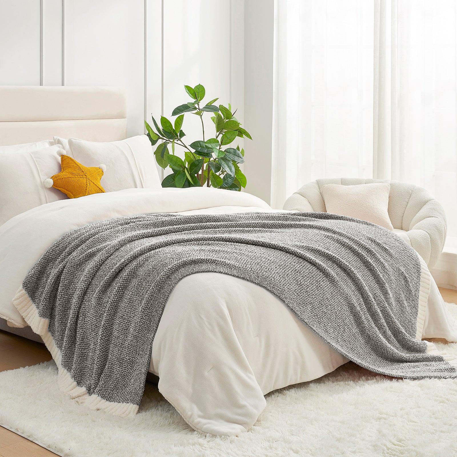 Gray blanket draped over a bed in a bright bedroom with a plant and window.  #color_Dark Grey