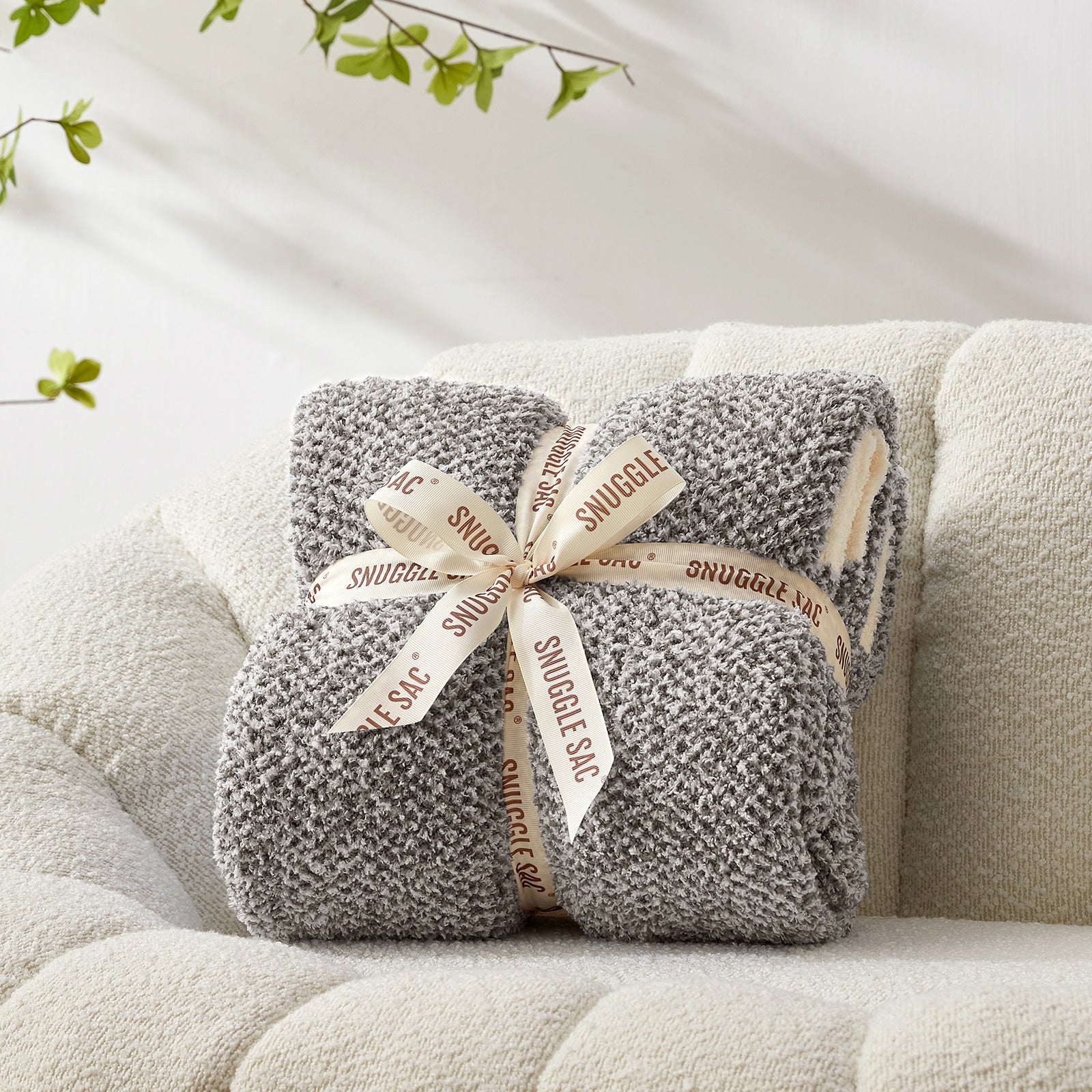 Gray plush blanket with a decorative bow on a beige couch  #color_Dark Grey
